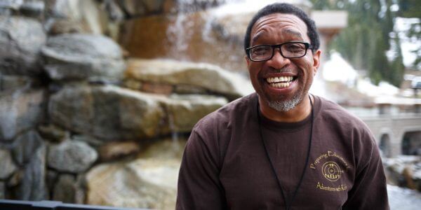 Darryl Haddock standing and smiling in front of a rock wall with trees in the background.