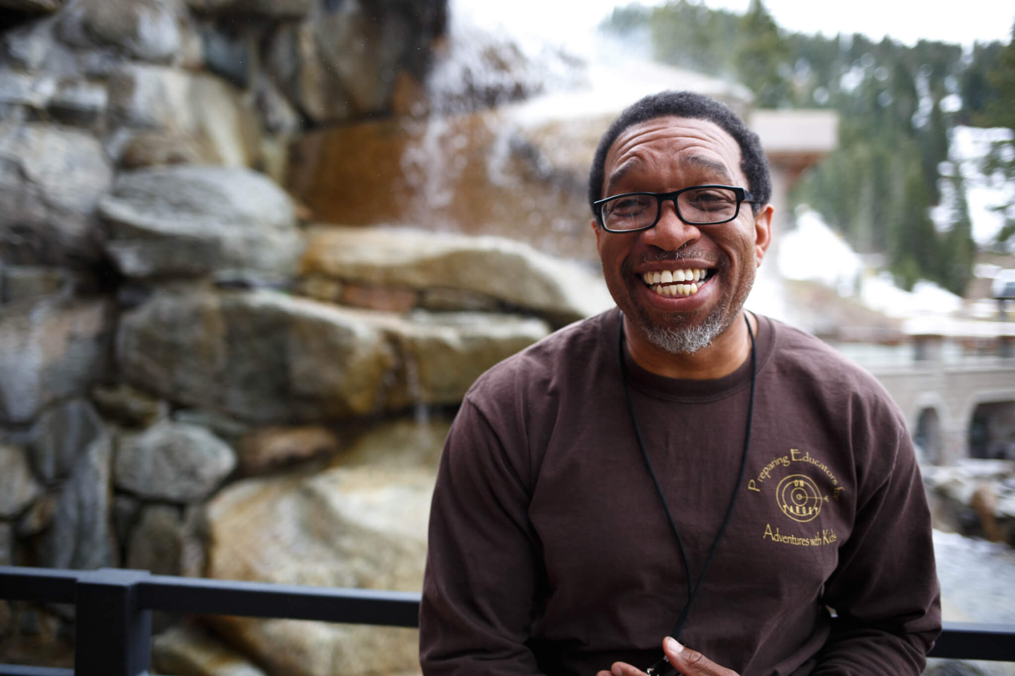 Darryl Haddock standing and smiling in front of a rock wall with trees in the background.