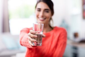 Young woman showing drinking glass with water