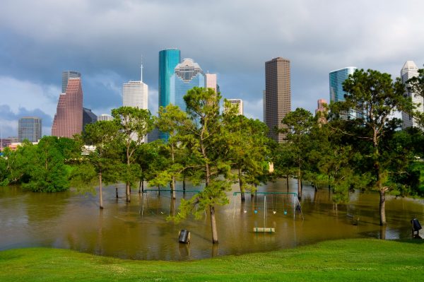 A flooded park with trees and swing sets, set against the Houston, Texas skyline.