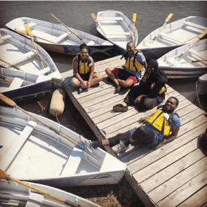 Four volunteers in life vests sitting on a dock with white boats nearby