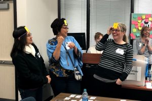 Three women at a training in a conference room laugh while doing an interactive learning activity.