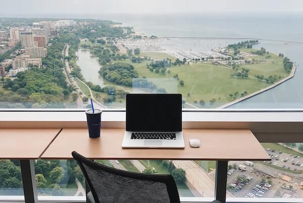 Laptop, mouse, and water cup with straw sitting on a desk overlooking the city of Milkwaukie.