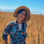 Fatuma Emmad stands in front of a field of golden wheat, wearing a hat and blue patterned shirt.