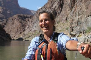 Nicole Silk in a canyon paddling a raft and smiling.