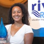 Mariah Davis (she/her) standing in front of the podium on the River Rally stage holding her Emerging Leader award.