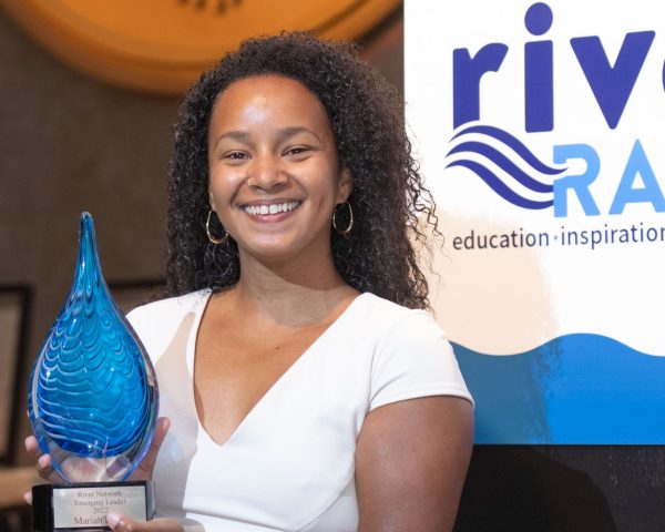 Mariah Davis (she/her) standing in front of the podium on the River Rally stage holding her Emerging Leader award.