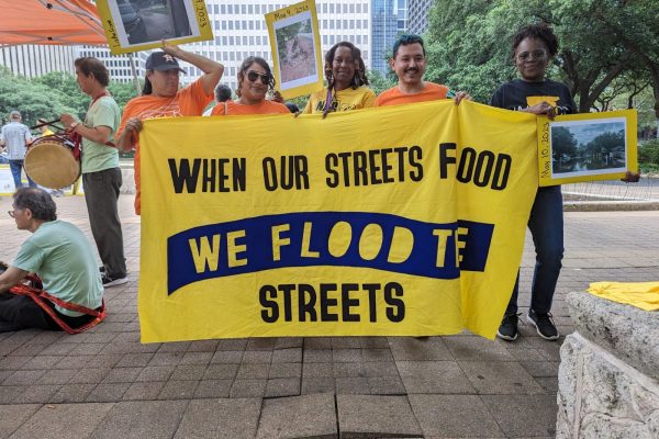 Five advocates stand in a city plaza holding a yellow sign that reads "When our streets flood we flood the streets."