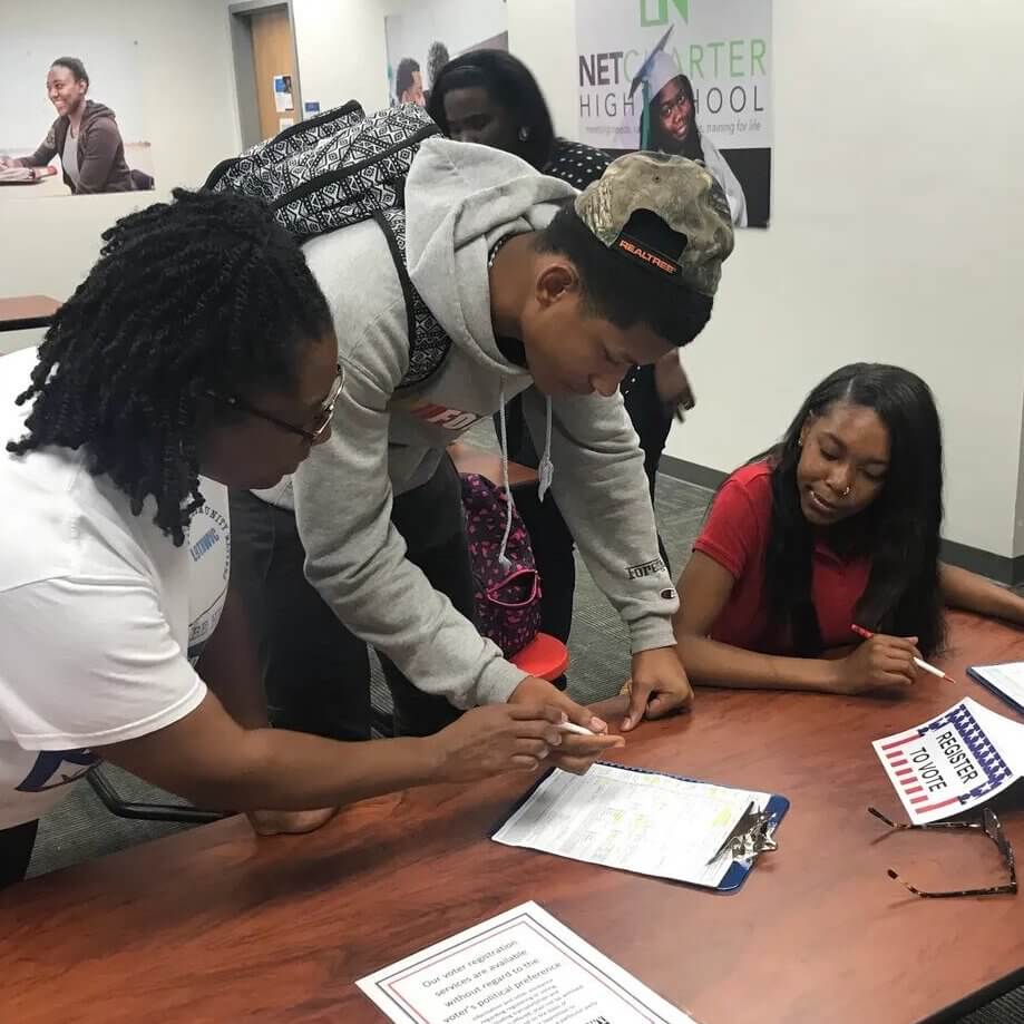 Shawon Bernard helps register two young black voters who are seated at a table.