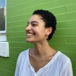 Campbell Simmons smiling off to the side, standing in front of a green brick wall.