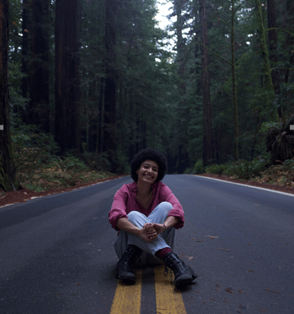 Campbell Simmons sits on the double yellow lines of a road in a forest with tall trees all around.