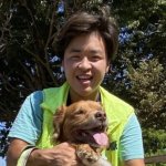 Max Suwaki wearing a yellow It Is Overdue vest, smiling with his dog.