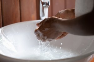 Photo of a person's hands being washed under running water in a white basin sink.