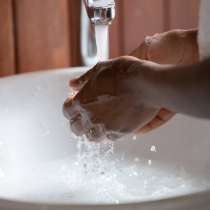 Photo of a person's hands being washed under running water in a white basin sink.