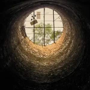 a photo of a well from below, looking up through a grate to the sky.