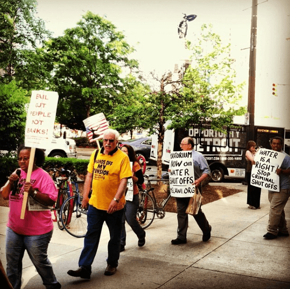 A photo of people walking and holding signs rallying against water shutoffs in Detroit, MI in 2014.